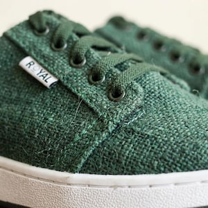 May include: Close-up of green canvas trainers with white soles. The trainers have green laces and eyelets. A small white tag with the word "ROYAL" is visible on the side of the shoe.