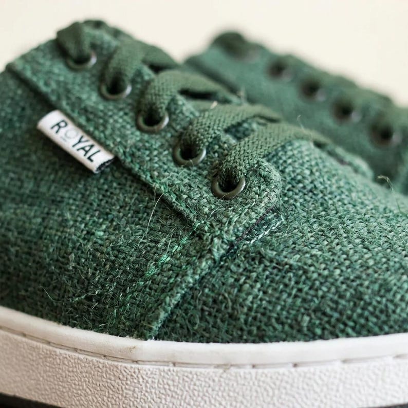 May include: Close-up of green canvas trainers with white soles. The trainers have green laces and eyelets. A small white tag with the word "ROYAL" is visible on the side of the shoe.
