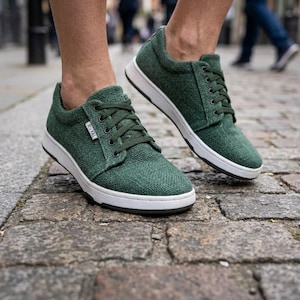 May include: Green trainers with white soles and dark green laces. The shoes have a textured fabric upper and a low-profile design. The shoes are shown on a cobbled street. The brand name "ROYAL" is visible on the side of the shoe.