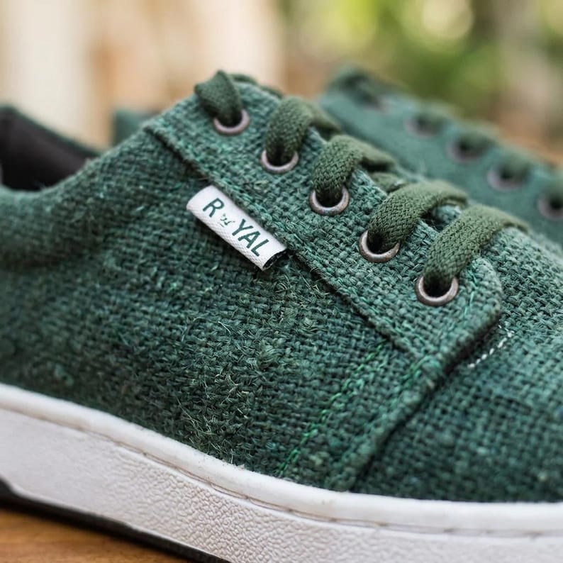 May include: Close-up of green canvas trainers with white soles. The trainers have green laces and eyelets. A small white tag with the word "ROYAL" is visible on the side. The shoes are made of a textured material.