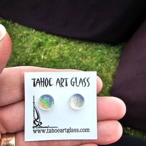 May include: A pair of iridescent glass stud earrings on a white card. The earrings are round with a shimmering, multicolored surface. The card reads "TAHOE ART GLASS" and includes a website address.