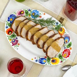Può includere: Un vassoio ovale con un colorato motivo floreale contiene carne a fette condita con salsa. Sono visibili anche un rametto di aneto e un bicchiere di liquido rosso.