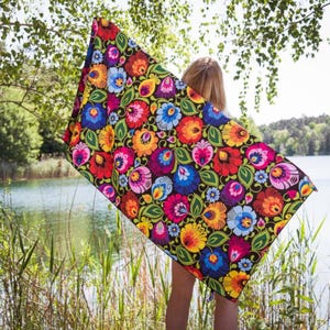 Könnte beinhalten: Ein farbenfrohes Strandtuch mit floralem Muster auf schwarzem Hintergrund. Das Design zeigt rote, gelbe, blaue und violette Blumen mit grünen Blättern. Das Tuch wird in der Nähe eines Sees gehalten.