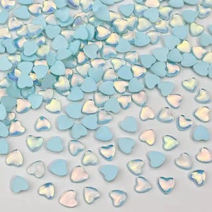 May include: A scattering of small, heart-shaped embellishments. The hearts are a soft, pastel blue color, with some featuring an iridescent, shimmering effect. These decorative elements are ideal for crafts and DIY projects.