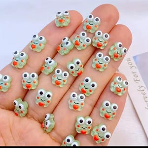May include: A collection of green frog-shaped resin embellishments with white eyes and red hearts. The frog embellishments are perfect for adding a whimsical touch to crafts, jewelry, and other projects.