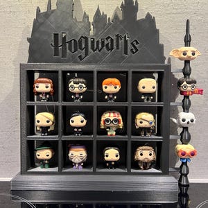 May include: Black Hogwarts themed display stand with 16 square compartments, each holding a small figurine. The stand features a silhouette of Hogwarts castle with the word "Hogwarts" printed on the front. A separate vertical stand holds four additional figurines.