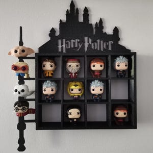 May include: A black wall shelf with a Harry Potter silhouette and 12 compartments. The shelf is filled with Funko Pop figures of Harry Potter characters, including Harry Potter, Hermione Granger, Ron Weasley, Dumbledore, and more.