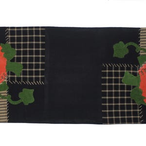 Puede incluir: Un camino de mesa negro con un tema de calabaza. El camino de mesa presenta un gran panel central negro, con secciones de tela a cuadros y a rayas. Las calabazas naranjas con hojas verdes est&aacute;n aplicadas en los lados.