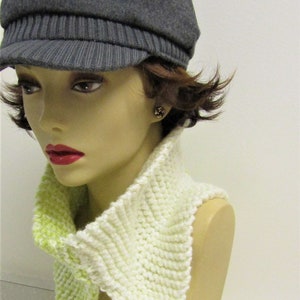 May include: A white and lime green knitted cowl neck scarf. The scarf is worn by a mannequin with a gray newsboy cap.