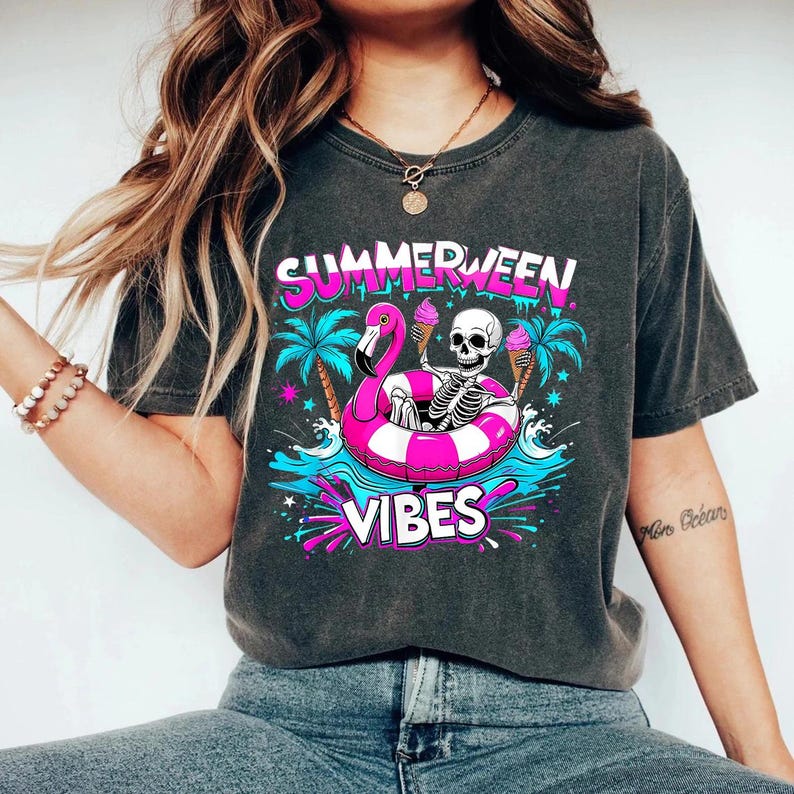 May include: Dark gray t-shirt with a colorful graphic. The graphic features a skeleton in a pink flamingo floatie, palm trees, and the words "SUMMERWEEN VIBES". The skeleton holds two ice cream cones.