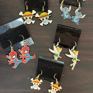 May include: Assortment of colorful cartoon character earrings.  The earrings feature characters like Stitch, Tinkerbell, Spiderman, and a skull with a straw hat.