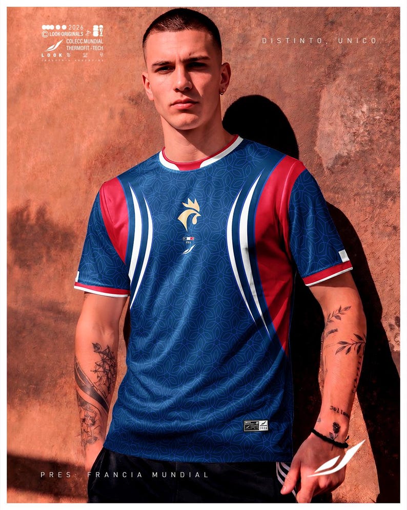 K&ouml;nnte beinhalten: Ein kurz&auml;rmeliges Sporttrikot in Blau, Rot und Wei&szlig; mit einem sich wiederholenden geometrischen Muster. Auf der Brust befindet sich ein goldenes Hahn-Emblem &uuml;ber einer kleinen franz&ouml;sischen Flagge. Der Text umfasst "2026", "LOOK ORIGINALS", "COLECC.MUNDIAL", "THERMOFIT-TECH", "DISTINTO. UNICO" und "PRES: FRANCIA MUNDIAL".