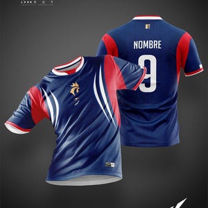 K&ouml;nnte beinhalten: Ein marineblaues Fu&szlig;balltrikot mit roten &Auml;rmeln und geschwungenen wei&szlig;en Seitenstreifen. Die Vorderseite zeigt ein goldenes Hahn-Emblem und die R&uuml;ckseite den Text NOMBRE &uuml;ber der wei&szlig;en Nummer 9. Der Stoff hat ein dezentes geometrisches Muster.