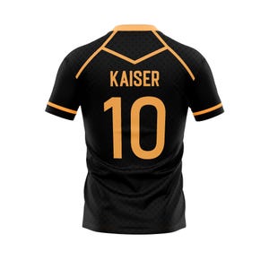 以下が含まれることがあります： オレンジ色のアクセントが付いた黒色のスポーツジャージ。背中には「KAISER」という名前と「10」の数字がオレンジ色で表示されています。襟と袖口にはオレンジ色のトリムが付いています。ジャージはテクスチャード加工された生地で作られています。