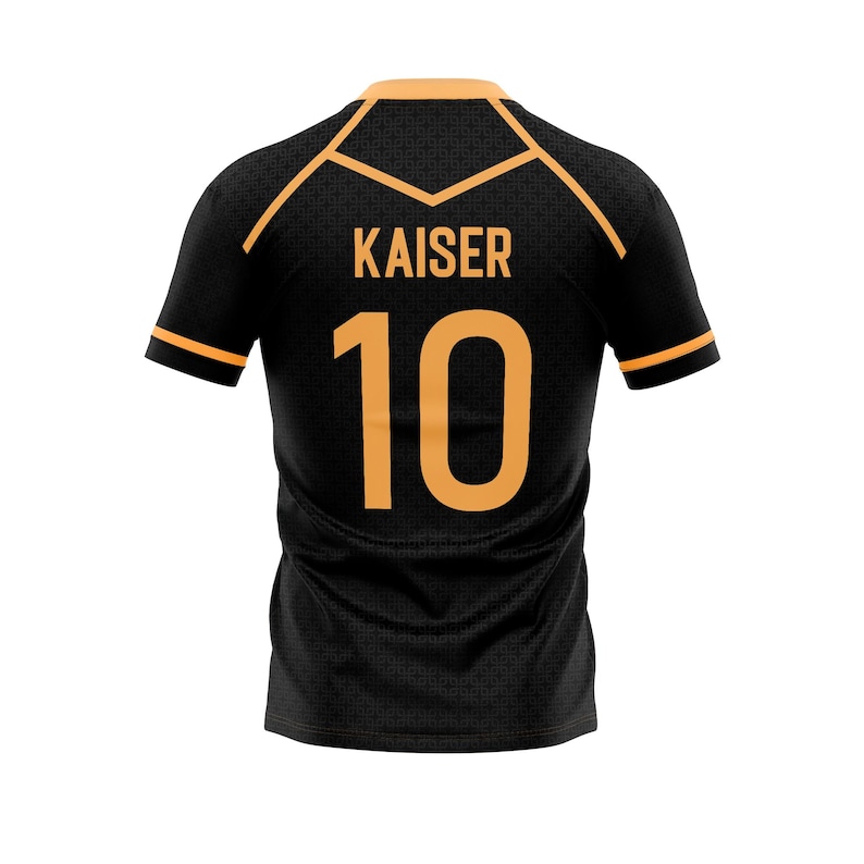 以下が含まれることがあります： オレンジ色のアクセントが付いた黒色のスポーツジャージ。背中には「KAISER」という名前と「10」の数字がオレンジ色で表示されています。襟と袖口にはオレンジ色のトリムが付いています。ジャージはテクスチャード加工された生地で作られています。