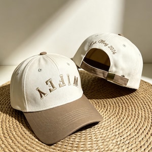 Peut inclure: Deux casquettes de baseball blanches avec des visières marron. L'une porte le mot "WIFEY" brodé en marron. L'autre porte "Est. May 2024" brodé en marron. Les casquettes sont posées sur une surface tissée.