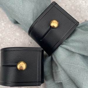 Miller & Jeeves: Two black leather napkin rings with brass stud fastening.