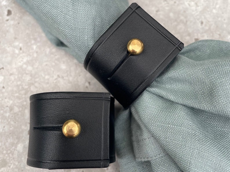 Miller & Jeeves: Two black leather napkin rings with brass stud fastening.