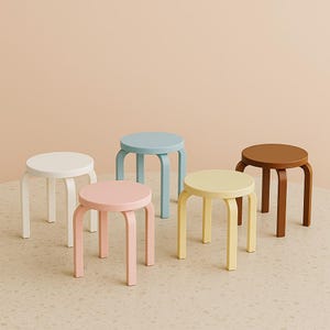 May include: Five wooden stools in different colours: white, light blue, light pink, light yellow, and brown. The stools have a simple design with four legs and a round seat.