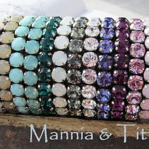 Peut inclure: Un ensemble de bracelets colorés faits de petits cristaux ronds. Les bracelets sont disposés en dégradé de turquoise à violet. Le texte "Mannia & Titta" est visible en bas de l'image.