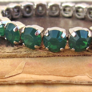 May include: A silver stretch bracelet with emerald green rhinestones. The bracelet is on top of a stack of old books.