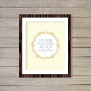 May include: A framed print with a yellow and white striped background. A wreath of seashells, starfish, and seaweed surrounds the text "sea shells in my pocket and sand in my toe".