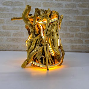 Op de afbeelding: Handgemaakte houten lamp met een natuurlijk ontwerp. De lamp heeft verweven takken en een warm, gloeiend licht. Het hout heeft een gouden tint en het licht is zachtgeel. Uniek decoratie-item.