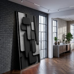 Peut inclure: Œuvre d'art murale abstraite avec un motif géométrique de rectangles superposés en nuances de gris et de noir. L'œuvre a un aspect texturé et est exposée dans un cadre intérieur moderne, adossée à un mur de briques sombres.
