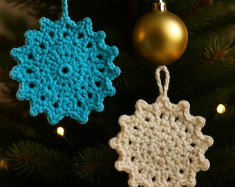 Puede incluir: Dos adornos de copos de nieve hechos a mano con ganchillo. Uno es de color azul turquesa brillante y el otro blanco roto. Ambos cuelgan de un árbol de Navidad. También se ve una bola dorada. Los copos de nieve miden unos 10 cm de diámetro.