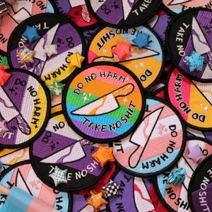 May include: A selection of embroidered patches with the slogans "DO NO HARM" and "TAKE NO SHIT". The patches feature a knife graphic and rainbow, purple, and yellow backgrounds. Some patches have star-shaped embellishments.