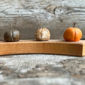 May include: Three small decorative gourds on a wooden shelf. The gourds are different colors and textures. One is brown and has a rough texture, one is white with a smooth texture, and one is orange with a smooth texture.