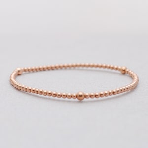 May include: A delicate rose gold beaded bracelet with three larger beads spaced evenly around the bracelet.