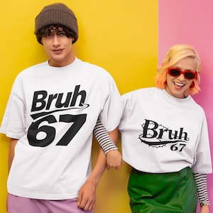 May include: Two people wearing white t-shirts with the text "Bruh 67" in black. One shirt has a stylized design above the text. The background is split between yellow and pink. One person wears a brown beanie.