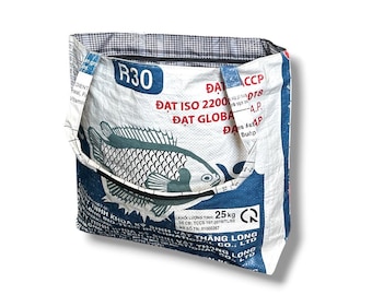 May include: A tote bag constructed from a repurposed white and blue woven plastic feed sack. The exterior features a graphic of a fish, the text R30, and various printed technical specifications. The interior is lined with a black and white plaid fabric.