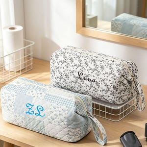 May include: Two quilted cosmetic bags. One is white with a floral pattern and the name "Luna" embroidered in black. The other is light blue with a patchwork design and the initials "ZL" embroidered in blue. Both have zipper closures.