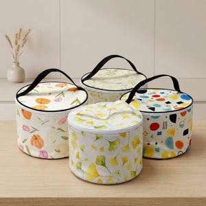 May include: Four round, zippered storage containers with black handles. One features orange pumpkins and pink tulips, one has yellow ginkgo leaves, one displays a light botanical pattern, and one shows a colorful geometric print on white.