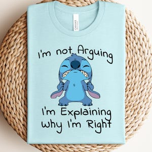 May include: Light blue t-shirt featuring a cartoon character with the text "I'm not Arguing, I'm Explaining why I'm Right". The graphic shows a blue alien-like creature with a grumpy expression.
