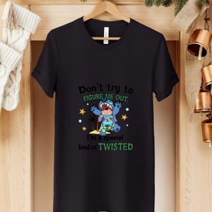 May include: Black t-shirt featuring a cartoon character with the text "Don't try to figure me out. I'm a special kind of TWISTED." The character is blue with a wide open mouth and wearing a Hawaiian shirt.