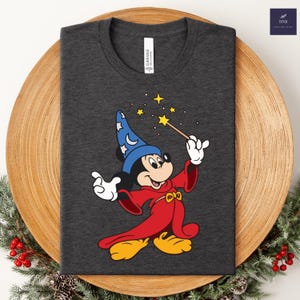 Puede incluir: Camiseta gris oscuro con un dise&ntilde;o de Mickey Mouse de dibujos animados vestido de mago. Mickey lleva un sombrero azul con lunas y estrellas, una t&uacute;nica roja y zapatos amarillos. Sostiene una varita con una estrella, con estrellas encima.