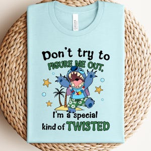 May include: Light blue t-shirt featuring a cartoon character with the text "Don't try to figure me out, I'm a special kind of twisted." The character is blue with large ears, wearing floral shorts and a lei.