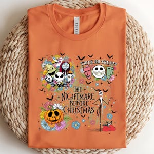May include: Orange t-shirt featuring characters and imagery from The Nightmare Before Christmas. The design includes Jack Skellington, Sally, and other characters, along with the text "Trick or Treat?" and "The Nightmare Before Christmas."