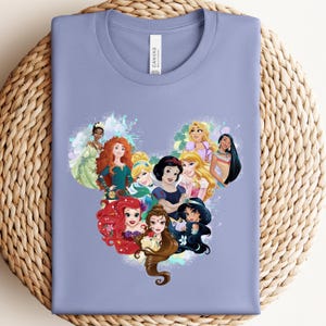 K&ouml;nnte beinhalten: Ein helllila T-Shirt mit einem herzf&ouml;rmigen Design aus Cartoon-Prinzessinnen. Die Prinzessinnen sind in leuchtenden Farben dargestellt, mit detaillierten Gesichtsz&uuml;gen und Kleidung. Das T-Shirt hat einen klassischen Rundhalsausschnitt und kurze &Auml;rmel.