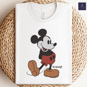 May include: White t-shirt with a black and white image of Mickey Mouse wearing red shorts and black shoes. The text "DISNEY" is printed in black below Mickey Mouse.