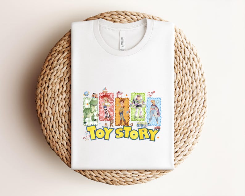 Puede incluir: Camiseta blanca con un gr&aacute;fico colorido de personajes de la pel&iacute;cula "Toy Story". El dise&ntilde;o incluye a Woody, Buzz Lightyear y otros personajes, con las palabras "Toy Story" en amarillo y azul.