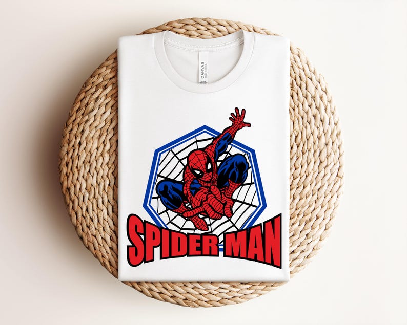May include: White t-shirt featuring a graphic of Spider-Man in a web design, with the word "SPIDER-MAN" in red block letters. The superhero is depicted in his classic red and blue suit.
