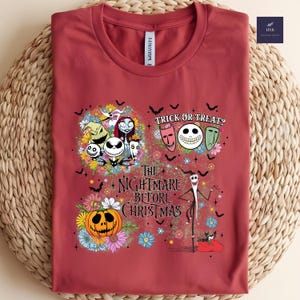 May include: A maroon t-shirt featuring a colorful graphic from "The Nightmare Before Christmas." The design includes Jack Skellington, Sally, Zero, and other characters, along with the text "Trick or Treat?" and "The Nightmare Before Christmas."