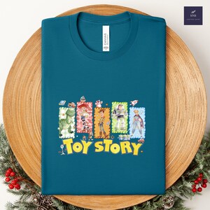 Puede incluir: Camiseta de color turquesa con un gr&aacute;fico colorido de los personajes de Toy Story. El dise&ntilde;o incluye im&aacute;genes de Rex, Jessie, Woody, Buzz Lightyear y otros, con las palabras "Toy Story" en amarillo. La camiseta es de material suave.