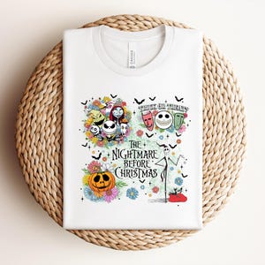 May include: White t-shirt featuring a colorful graphic from "The Nightmare Before Christmas." The design includes Jack Skellington, Sally, Zero, and other characters, along with the text "Trick or Treat" and "The Nightmare Before Christmas."