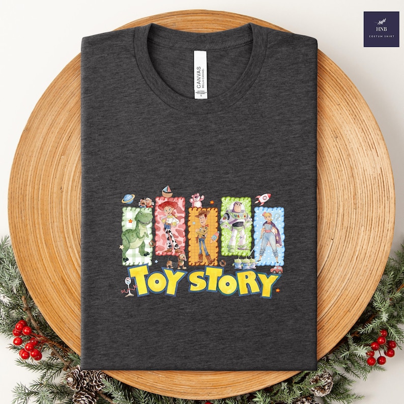 Puede incluir: Camiseta gris oscuro con un gr&aacute;fico colorido de personajes de la pel&iacute;cula "Toy Story". El dise&ntilde;o incluye im&aacute;genes de Woody, Buzz Lightyear y otros personajes, con las palabras "Toy Story" en amarillo.