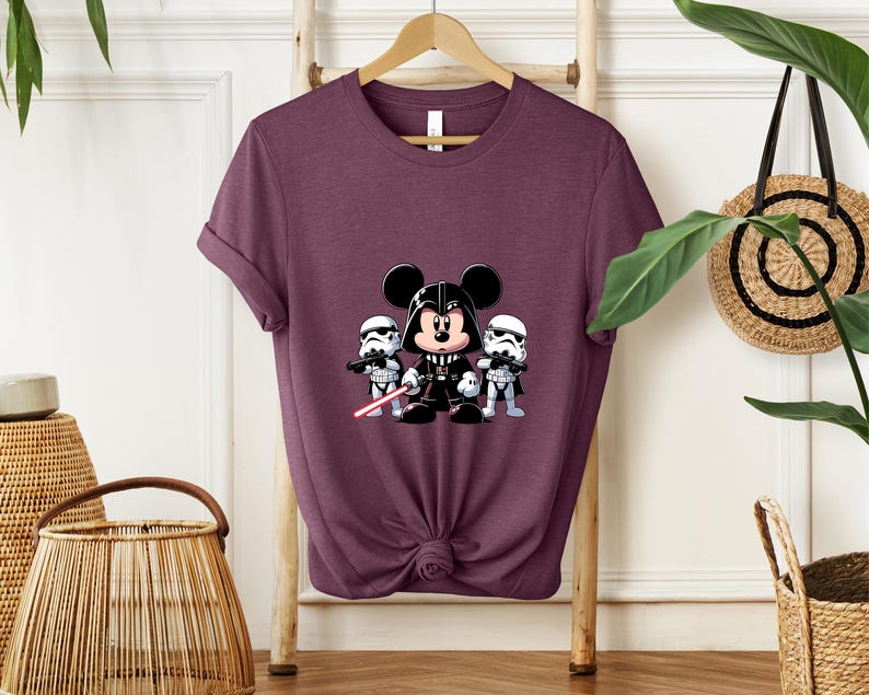 Pu&ograve; includere: T-shirt bordeaux con un disegno a cartoni animati di Topolino vestito da Darth Vader, affiancato da due Stormtrooper. Mickey tiene una spada laser rossa. Il disegno &egrave; centrato sulla parte anteriore della maglietta.